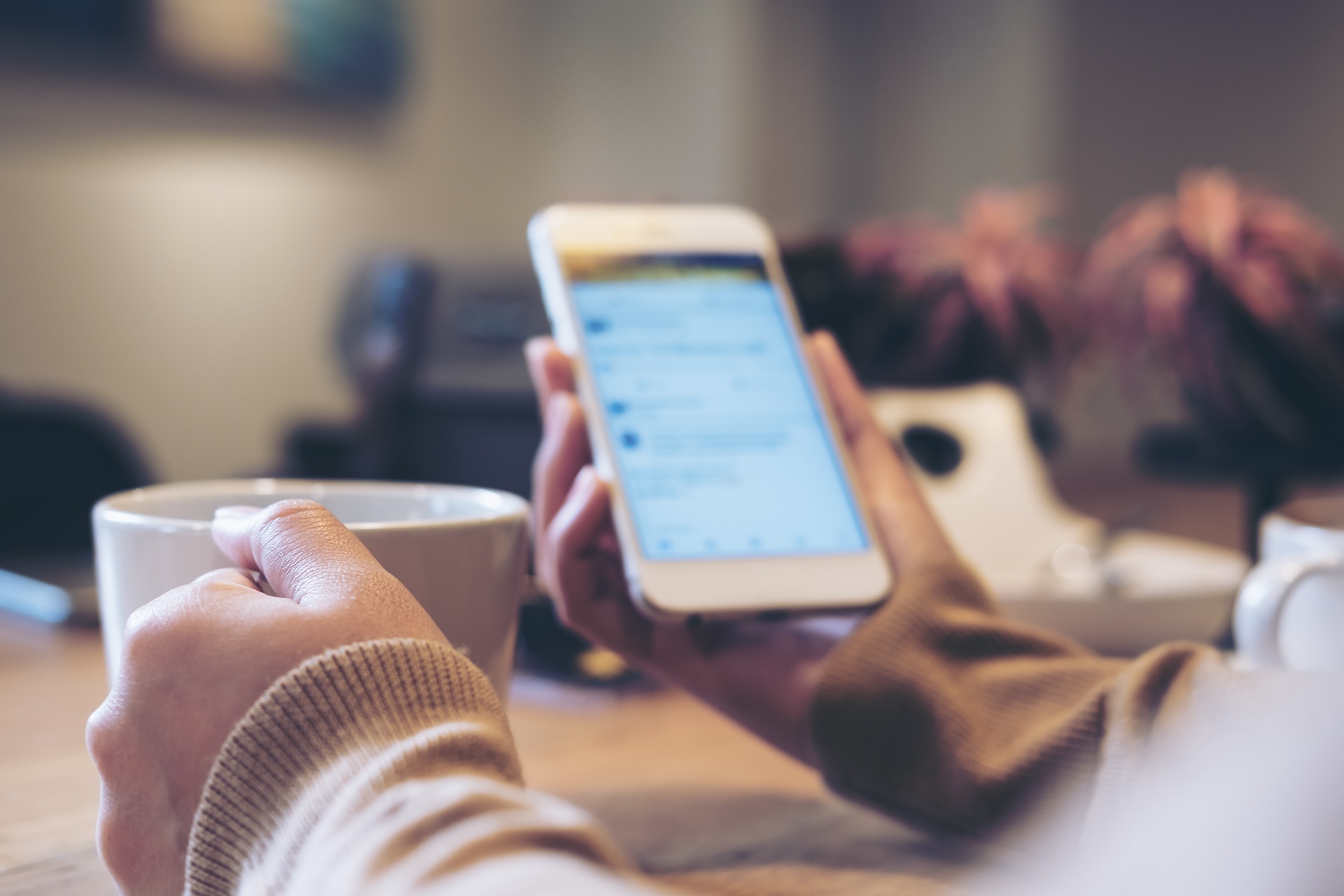 A woman's hands holding white coffee cup and mobile phone in modern loft cafe