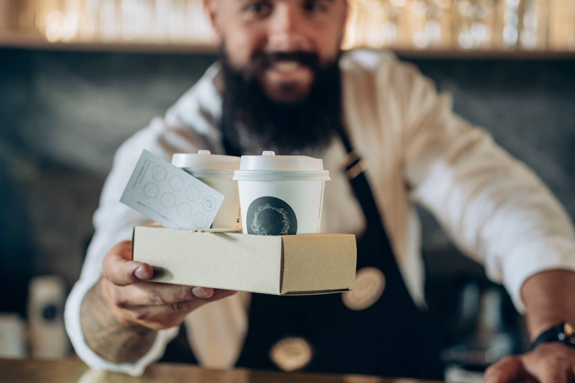 Smiling waiter giving tray with two cups of coffee with loyalty card