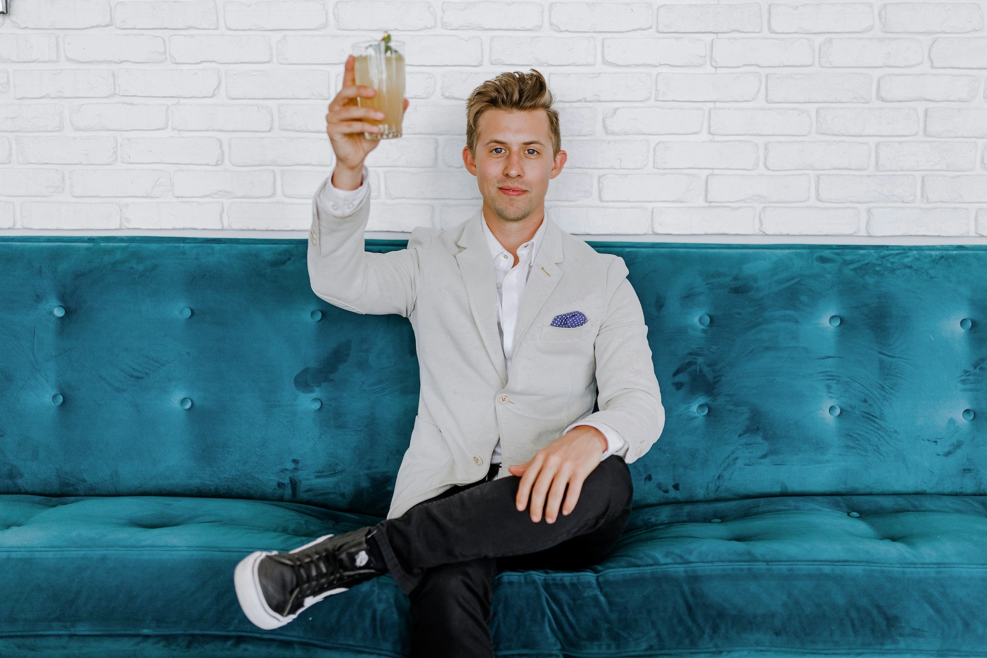 man in grey blazer raising drinking glass while sitting on sofa