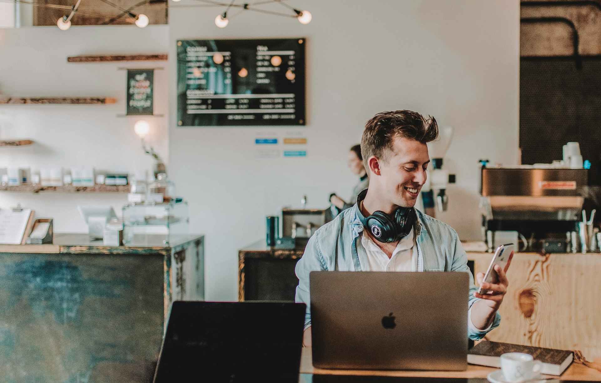 manager sitting at laptop in cafe smiling at phone