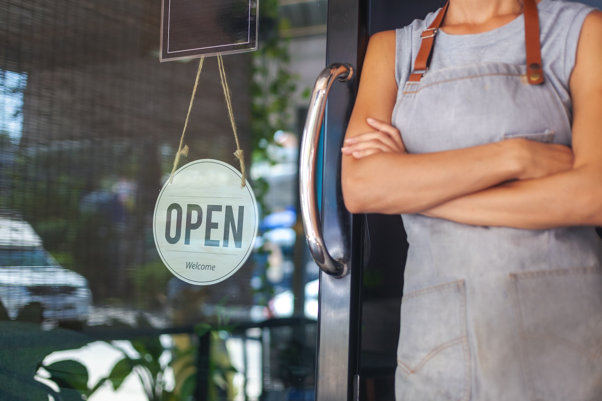 the owner of a quick service restaurant stands at the door with a sign Open
